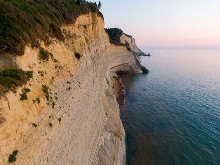 Dramatic cliffs meet a serene ocean at sunset.の写真素材