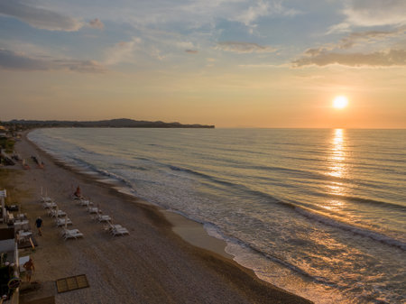 Golden sunrise over a tranquil beach with gentle waves and beach chairs.の写真素材