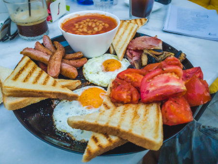 Full breakfast plate with eggs, sausages, bacon, beans, tomatoes, mushrooms, and toast.の写真素材