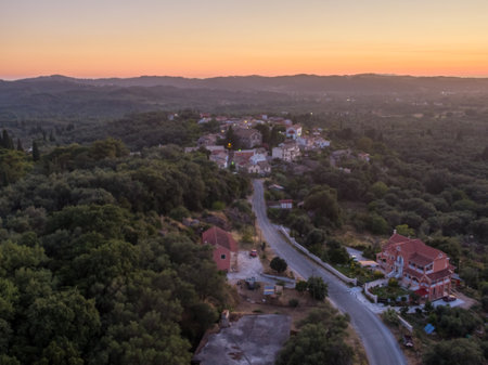 Aerial sunset view of a peaceful village nestled amidst rolling hills and lush greenery.の写真素材