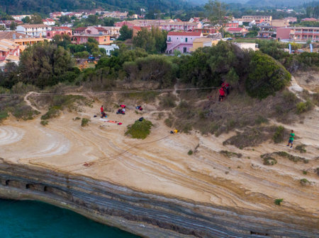 People setting up ropes and equipment on a cliff overlooking a town and turquoise water.