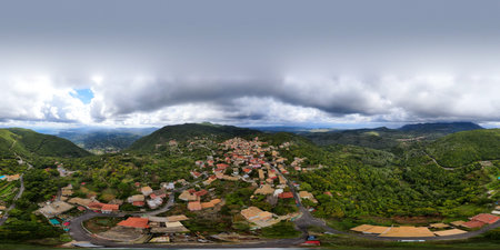 Hilltop village nestled in verdant mountains under a cloudy sky.の写真素材