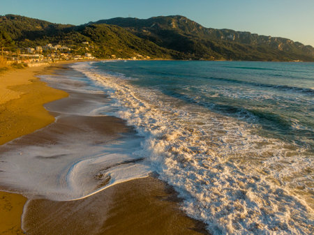 Golden sand meets turquoise waves on a tranquil beach, mountains in the background.の写真素材