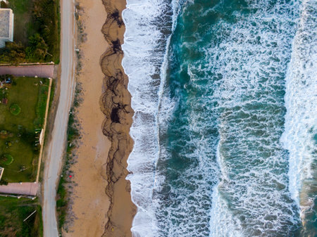 Aerial view of ocean waves crashing on sandy beach near houses.の写真素材