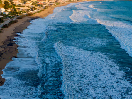 Ocean waves crashing on sandy beach near coastal townの写真素材