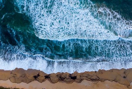 Aerial view of ocean waves crashing on sandy beach.の写真素材