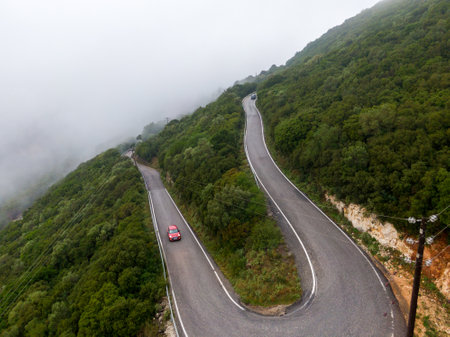 Winding mountain road through lush green landscape on a foggy day.の写真素材