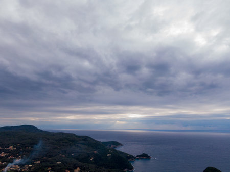 Coastal view under a dramatic, cloudy sky. Serene ocean meets lush green hills.の写真素材