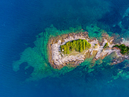 Aerial view of a small island in the ocean. Crystal clear waters surround the rocky coast.