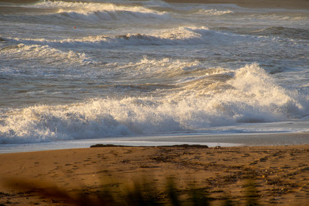 Waves crashing on a sandy beach, sunlight reflecting off the crests.