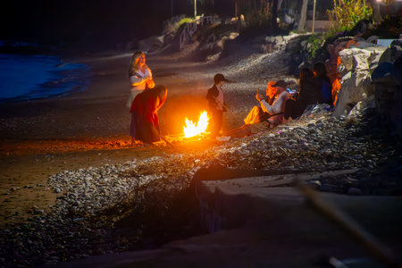 Beach bonfire at night casts warm glow on gathering of people enjoying each other's company.の写真素材