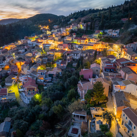 Aerial view of a hillside village aglow at dusk, nestled amongst trees with a mountain backdrop.の写真素材