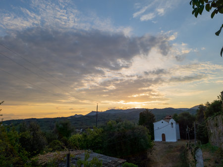 Scenic vista of a small white building nestled amidst lush greenery, basking in the warm glow of sunset.の写真素材