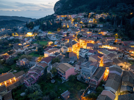 Twilight settles over a charming village nestled against a cliff, with lights twinkling in the darkness.の写真素材