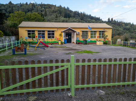 Sunny yellow building with a playground, nestled in a forest setting; likely a schoolhouse or community center.の写真素材
