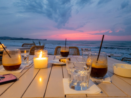 Sunset relaxation: Enjoying iced coffees by the sea, illuminated by a candle's soft glow. Tranquil beachの写真素材