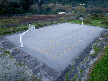 An aerial shot of a rectangular concrete basketball court with faded yellow lines and two white goals.の写真素材
