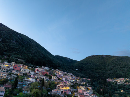 Scenic hillside village with colorful houses nestled amongst green mountains, bathed in twilight.の写真素材