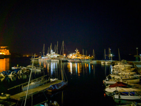 A captivating nightscape of a marina, showcasing yachts and smaller boats reflecting in the dark water.の写真素材