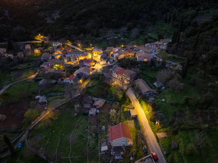 Aerial view of a quaint village nestled among rolling hills illuminated by warm streetlights at twilight.の写真素材