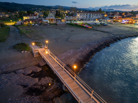 Illuminated pier stretching into the sea at twilight, with coastal town lights in the backgroundの写真素材