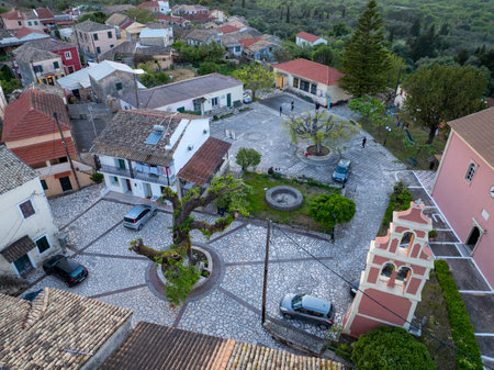 corfu, corfu, Greece. April 19, 2025: Aerial view of a quaint village square in Greece, featuring traditional architecture, parked cars, and a central tree.の写真素材