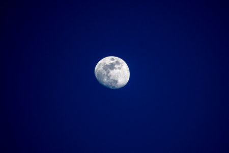 Full moon glows brightly against a dark blue night sky, illuminating the heavens.の写真素材