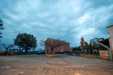 A view of a square in a European town, featuring a church, trees, and recreation area at twilight.の写真素材