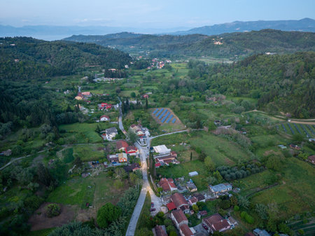 Aerial view of a serene countryside with houses, lush greenery, and rolling hills in the background.の写真素材
