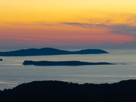 Golden hour casts a serene ambiance over distant islands, silhouetted against the tranquil sea.の写真素材