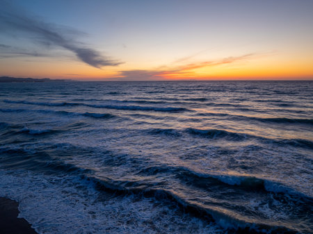 Sunset colors paint the sky as waves roll onto the beach, creating a tranquil and serene scene.の写真素材