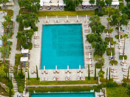 Aerial view captures a pristine swimming pool surrounded by loungers, parasols, and verdant foliage.の写真素材