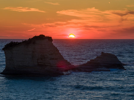 Oceanic sunrise showcases dramatic rock formations against a vibrant, colorful sky background.