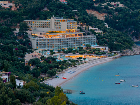 Coastal hotel resort at dusk, situated on a hillside overlooking a sandy beach and calm turquoise sea.の写真素材
