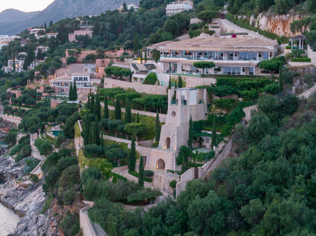 Luxury villa nestled on a lush hillside with terraces, gardens, and stunning coastal views below.の写真素材