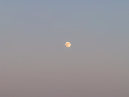 A serene full moon hovers gracefully against a soft gradient sky, casting a gentle glow. Peaceful night.の写真素材