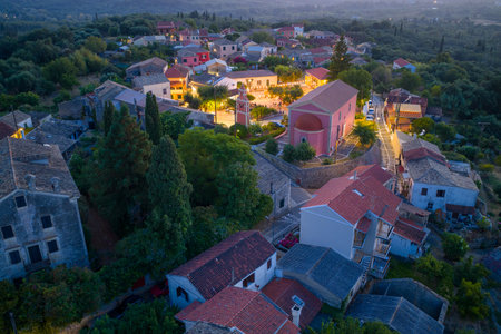 Aerial drone view of a picturesque Mediterranean village at twilight with church, stone rooftops, colorful houses, narrow streets and lush green hills in Corfu island Greeceの写真素材