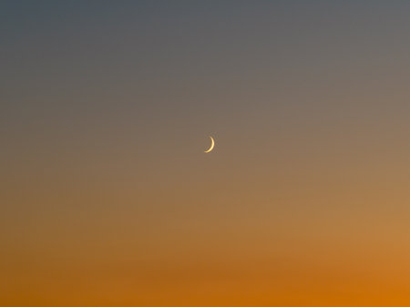 Crescent Moon in the Evening Sky: A serene and minimalist shot of a thin, glowing crescent moon set...