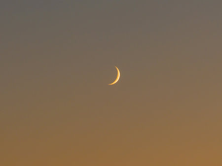 Crescent Moon in the Evening Sky: A serene and minimalist shot of a thin, glowing crescent moon set...