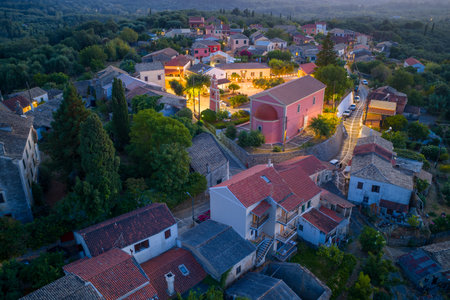Aerial drone view of a picturesque Mediterranean village at twilight with church, stone rooftops, colorful houses, narrow streets and lush green hills in Corfu island Greeceの写真素材