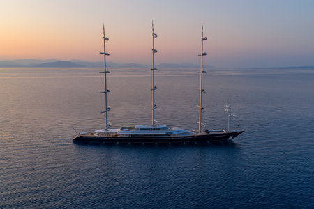 Aerial drone view of a magnificent three-mast luxury superyacht navigating serene blue ocean waters...