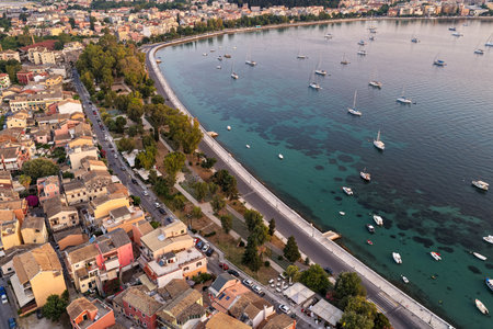 Aerial panoramic of the Corfu coastline and Garitsa Bay at sunrise with a vibrant sky, city buildings, and numerous boats.の写真素材