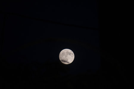 A brilliantly detailed full supermoon isolated against the pitch-black canvas of the night sky. A crisp, high-contrast telephoto shot showing the intricate craters and surface of the moonの写真素材