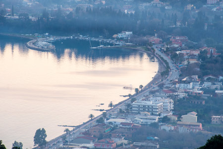 Breathtaking aerial view of the coastal town of Ipsos, Corfu, and its tranquil harbor at dawn. Soft morning light reflects on the calm Ionian Sea, veiled in a beautiful atmospheric haze.の写真素材