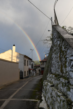 A magical rainbow arches over a narrow, wet alley in a quaint old European village after a rainstorm. Picturesque and atmospheric street scene with traditional houses and stone walls.の写真素材