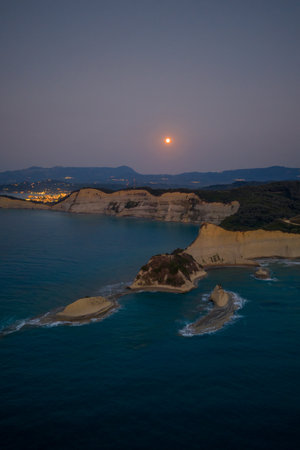 Aerial view of a full moon rising over the stunning coastal cliffs of Cape Drastis, Corfu. The...