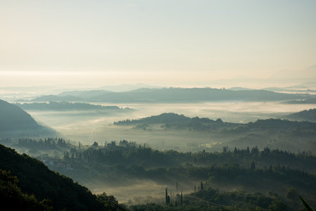 Ethereal sunrise over a misty, fog-filled valley in Corfu, Greece, with layers of hills and cypress treesの写真素材