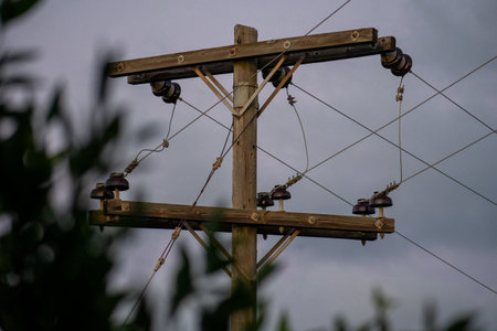 Old Wooden Utility Pole with Insulators and Wires Against a Cloudy Sky. Electric Power, Infrastructure, and Communication Technology Concept.の写真素材