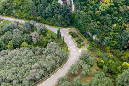 Aerial drone shot of a winding mountain road with a sharp curve through dense green forest in Corfu Greece travel transportation conceptの写真素材