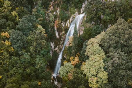 Vertical aerial shot of a hidden waterfall in Corfu Greece surrounded by dense forest with vibrant autumn foliage scenic nature travel backgroundの写真素材